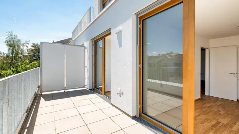 Heller Balkon mit Fliesenboden, Metallgeländer und Blick ins Grüne.