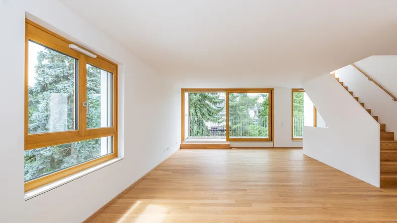 Helles und geräumiges Wohnzimmer mit großen Fenstern, Holzboden und Zugang zu einem Balkon.