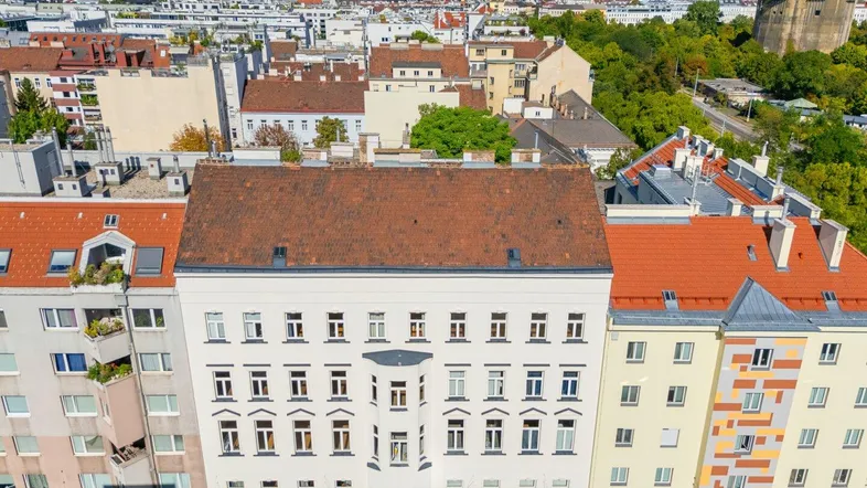 Luftaufnahme eines Wohngebäudes mit rotem Ziegeldach und Stadtpanorama im Hintergrund.