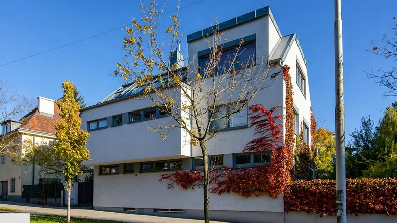 Modernes Wohnhaus mit weißer Fassade und herbstlicher Begrünung an der Straßenseite.