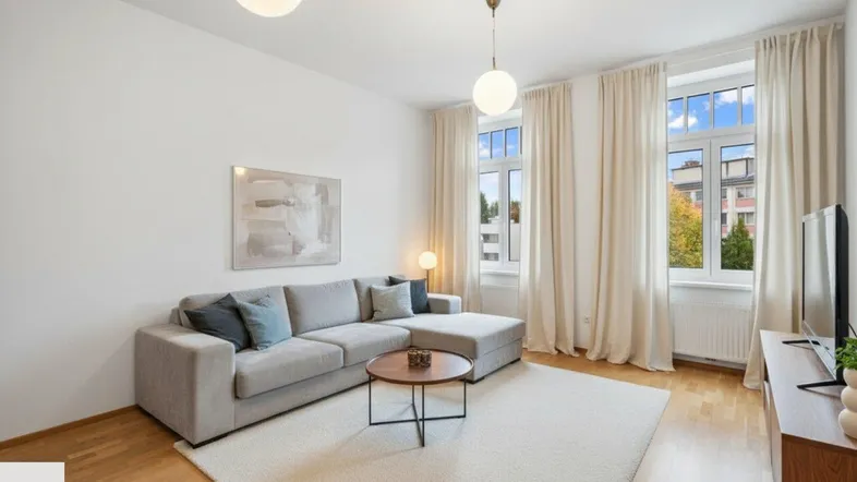 Helles Wohnzimmer mit modernem Sofa, Holzboden und großen Fenstern, die viel Tageslicht hereinlassen.