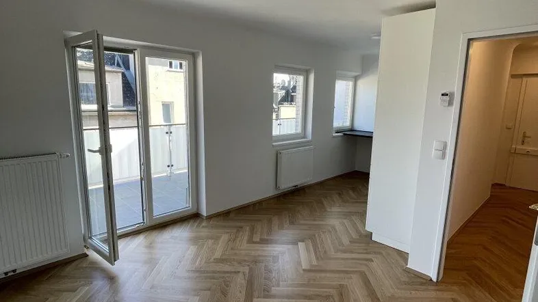 Helles Zimmer mit Fischgrätparkettboden und Zugang zu einem Balkon, ideal als Wohnbereich.