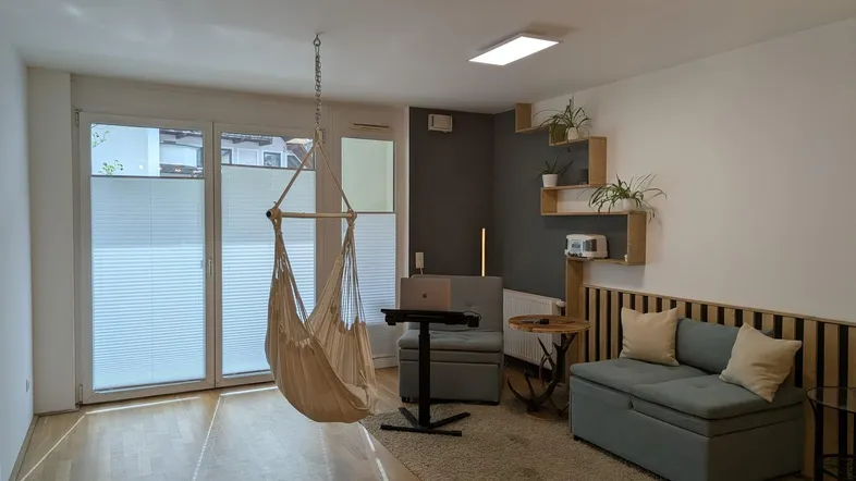 Helles Wohnzimmer mit Holzboden, Hängesessel und Zugang zu großen Fenstern.