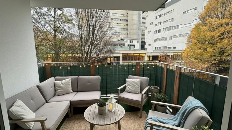 Gemütlicher Balkon mit bequemen Gartenmöbeln und Blick auf die umliegenden Gebäude und Bäume.