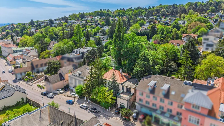 Luftaufnahme einer Wohngegend mit vielen Bäumen und Häusern in hügeliger Landschaft.