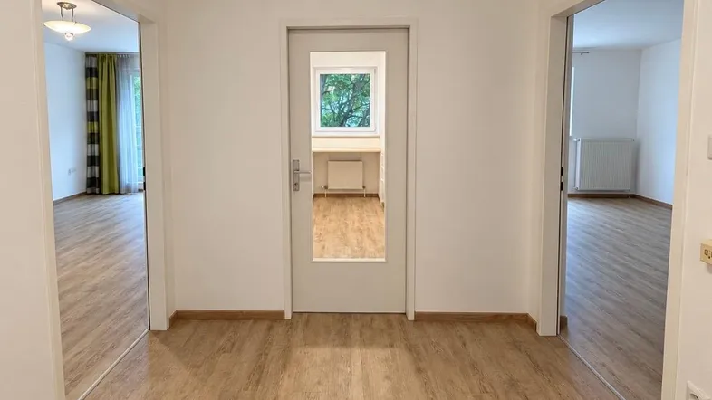 Heller Flur mit Laminatboden und Zugang zu verschiedenen Zimmern, inklusive Küche mit Fenster.