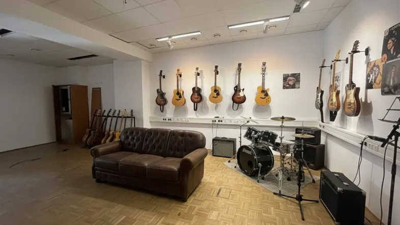 Geräumiger Musikraum mit verschiedenen Gitarren an der Wand, einem Schlagzeug und einem Ledersofa.