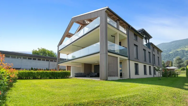 Modernes Mehrfamilienhaus mit Holzfassade, Glasbalkonen und gepflegtem Gartenbereich.