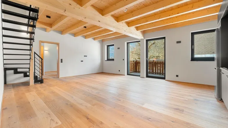 Helles, offenes Wohnzimmer mit Holzbalkendecke, Parkettboden und Zugang zum Balkon.