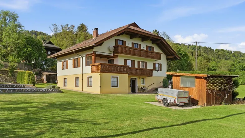 Traditionelles Haus mit Satteldach, Balkonen und großem grünen Garten in ländlicher Umgebung.