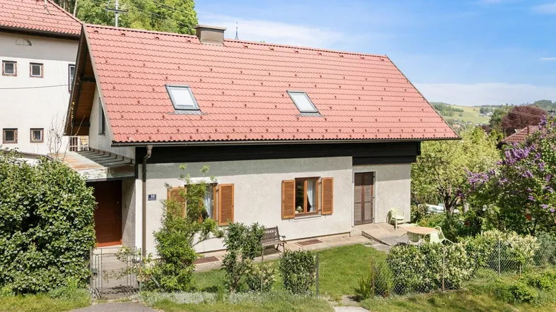 Traditionelles Einfamilienhaus mit rotem Ziegeldach, Garten und Blick auf die umliegende Landschaft.