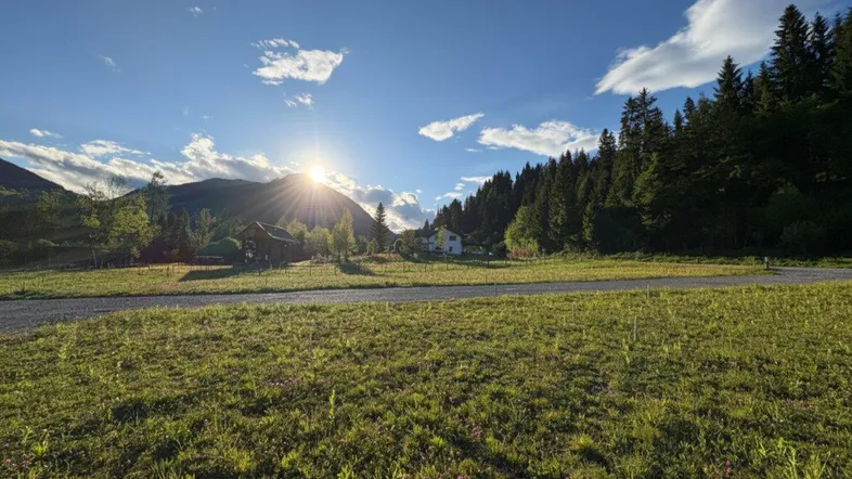 Weitläufige Landschaft mit Bergen, Wald und einem sonnigen Feld im Vordergrund bei Sonnenuntergang.
