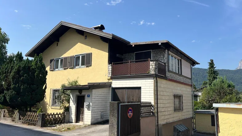 Ansicht des gelben Hauses mit Garage, Balkon und umliegender Vegetation an einem sonnigen Tag.