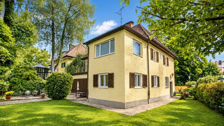 Traditionelles Haus mit gelber Fassade, braunen Fensterläden und gepflegtem Garten.