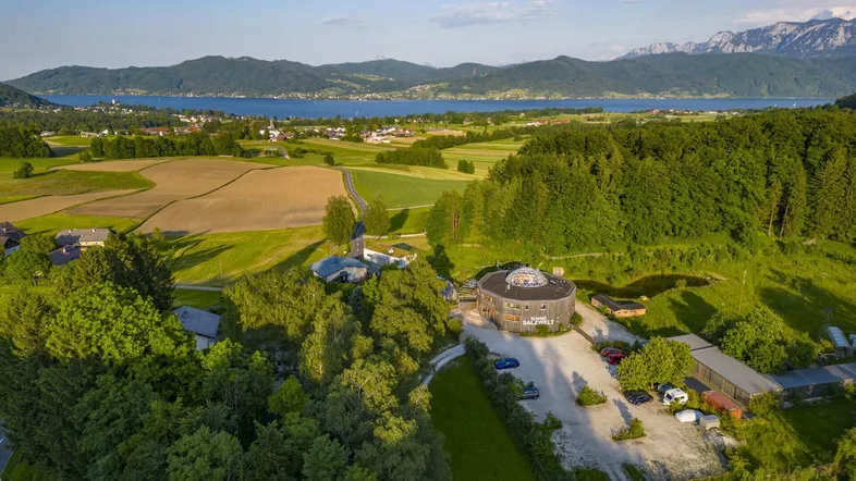 Luftaufnahme einer malerischen Landschaft mit See, Bergen und ländlicher Bebauung unter blauem Himmel.