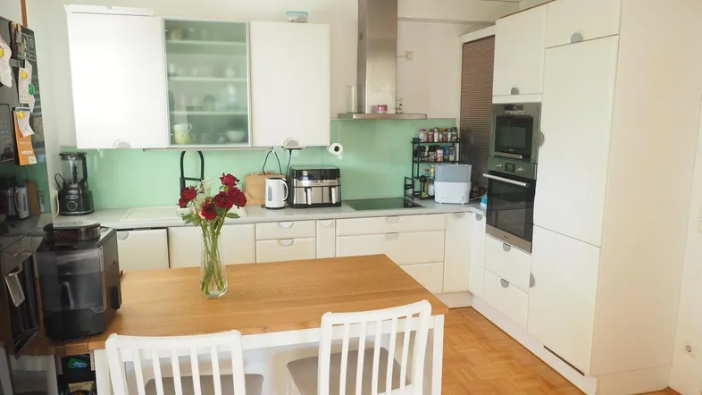 Moderne Einbauküche mit weißen Schränken, Holztisch und integrierten Geräten, ideal für Familienessen.