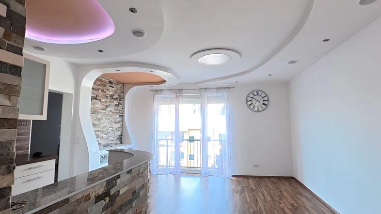 Helles Wohnzimmer mit modernem Deckenlicht, Holzboden und Zugang zum Balkon.