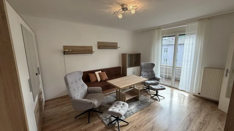 Helles Wohnzimmer mit Laminatboden, bequemen Sesseln und Zugang zum Balkon.