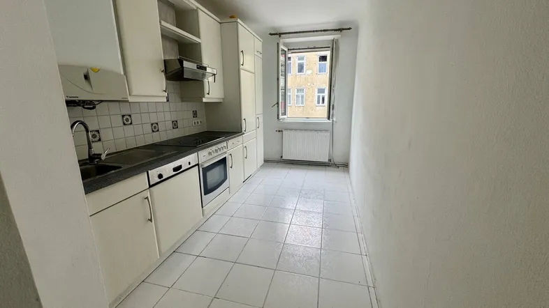 Schmale Küche mit weißen Einbauschränken, Fliesenboden und Blick auf die umliegenden Gebäude.