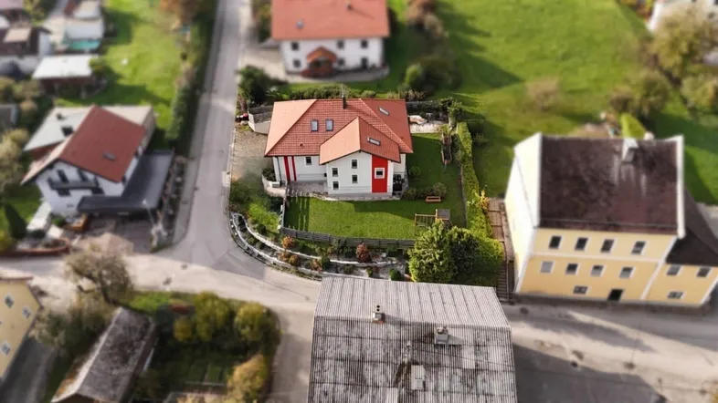 Luftaufnahme eines Einfamilienhauses mit rotem Dach und gepflegtem Garten in ländlicher Umgebung.