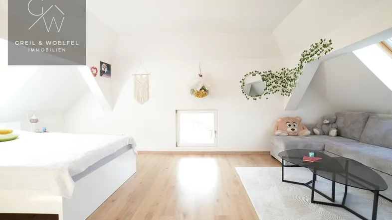 Helles Dachzimmer mit Bett, Sofa, Holzboden und schrägen Wänden, ideal als Schlaf- oder Jugendzimmer.