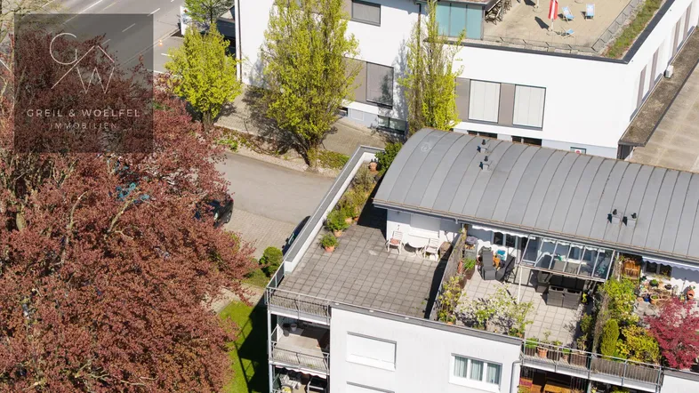 Luftaufnahme eines Gebäudes mit großer Dachterrasse und umliegender Wohnbebauung.