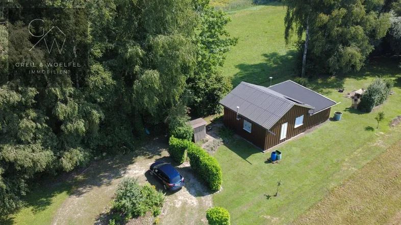 Luftaufnahme eines kleinen Hauses mit Garten, Parkplatz und angrenzenden Feldern.