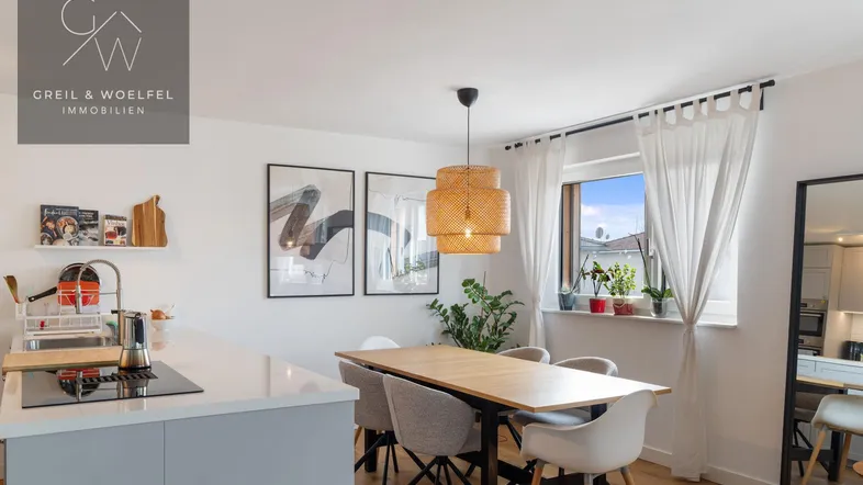 Essbereich mit Holztisch und moderner Kücheninsel, beleuchtet von einer stilvollen Hängelampe.