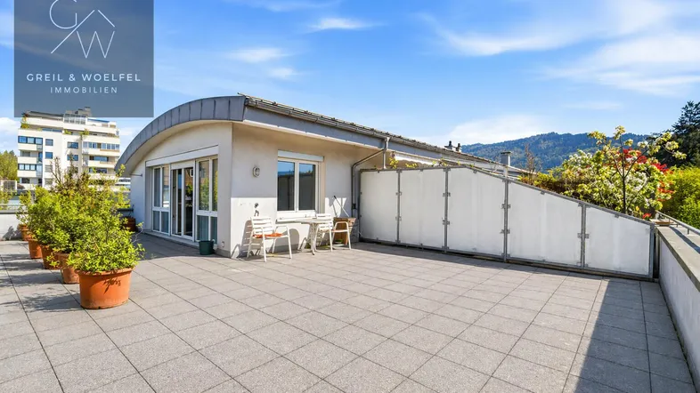 Große, sonnige Dachterrasse mit Fliesenboden und Sitzgelegenheiten, umgeben von grüner Landschaft.