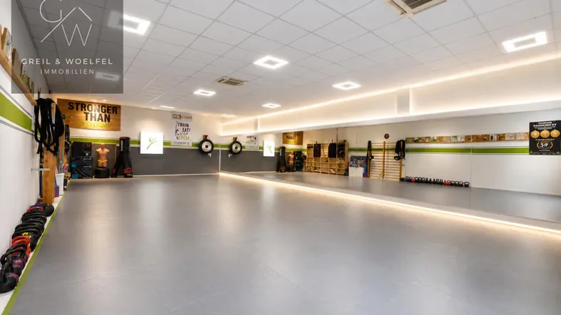 Großer, heller Raum mit grauem Boden und Spiegelfront, ideal für Fitness- oder Bewegungsstudios.