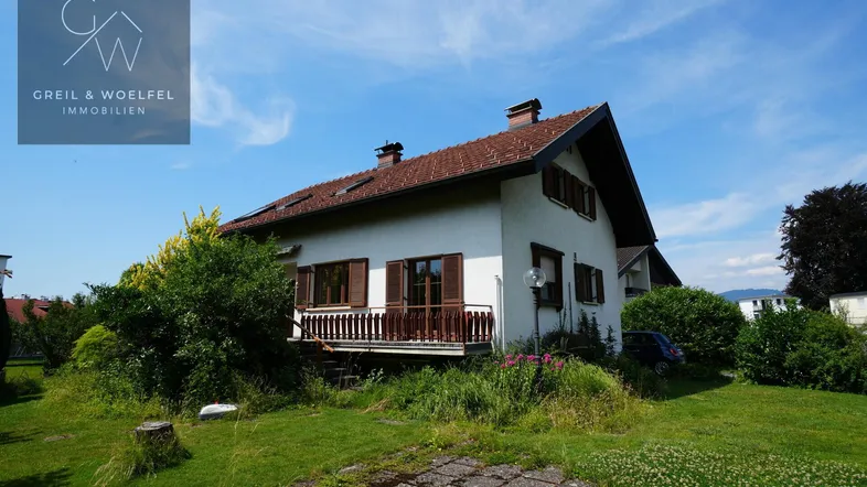 Freistehendes Einfamilienhaus mit Satteldach, Balkon und umgebendem Garten unter blauem Himmel.