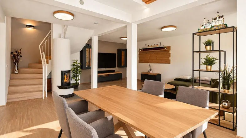 Heller, offener Wohn- und Essbereich mit Holzbalken, Kamin und Zugang zu einer Treppe.