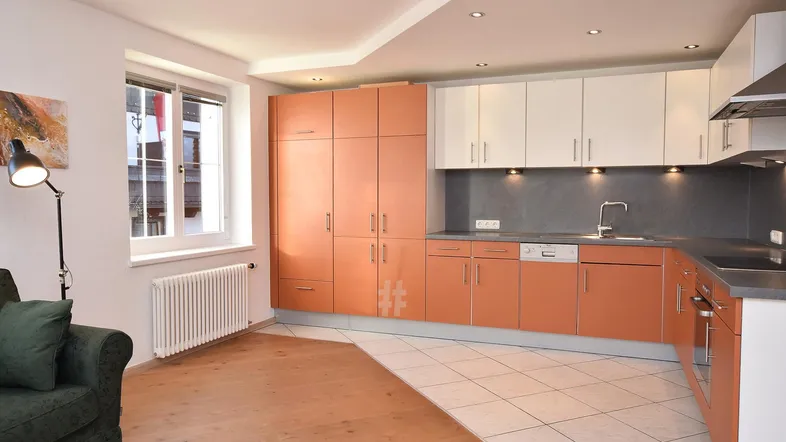 Helle Küche mit orangefarbenen und weißen Schränken, integriertem Geschirrspüler und Holzboden im Wohnbereich.