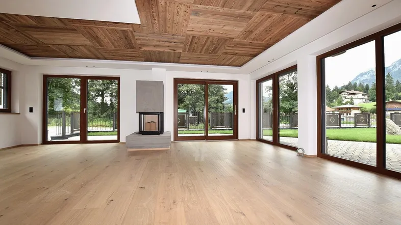 Geräumiges Wohnzimmer mit hellem Holzboden, Holzbalkendecke, modernem Kamin und Zugang zum Garten.