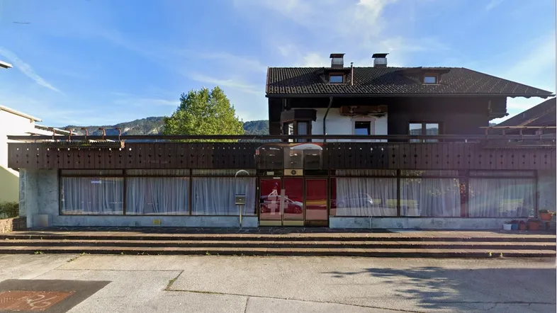 Traditionelles Gebäude mit Holzfassade und Balkon, umgeben von Bergen unter blauem Himmel.