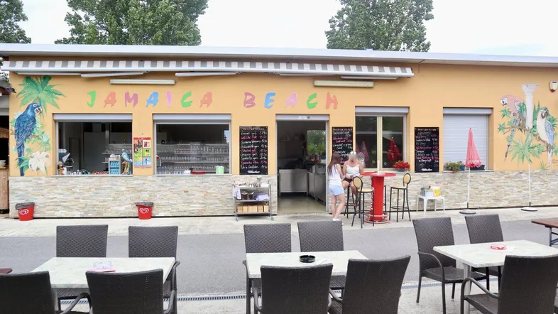 Gebäude mit "Jamaica Beach" Beschriftung und davorliegendem Außenbereich mit Tischen und Stühlen.