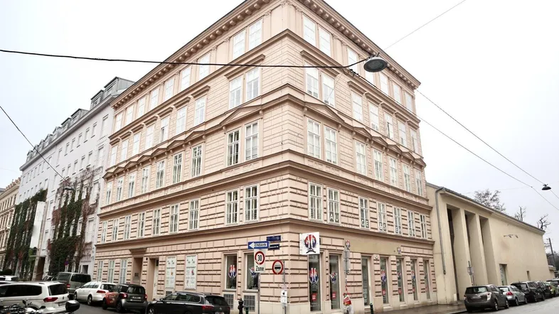 Klassisches Eckgebäude mit mehreren Etagen und traditioneller Fassadengestaltung an einer belebten Straße.
