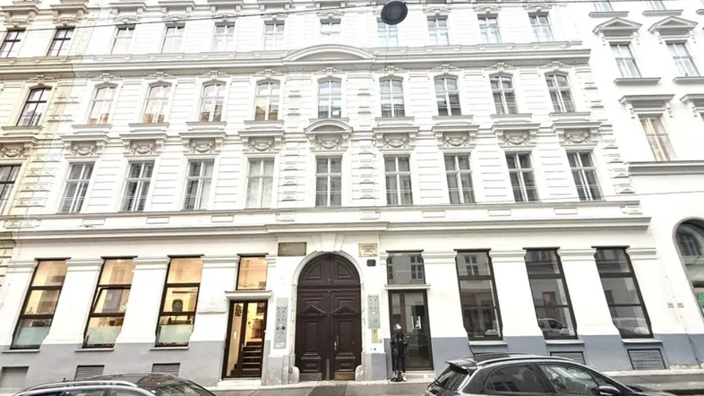 Historische Fassade eines Mehrfamilienhauses mit vielen Fenstern und geparkten Autos davor.