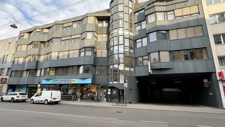 Modernes Geschäftsgebäude mit markanter Glasfassade und integriertem Supermarkt im Erdgeschossbereich.