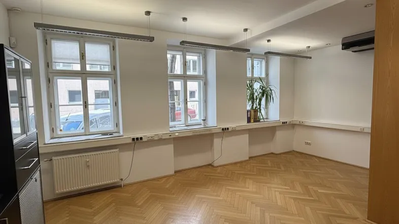Geräumiges Büro mit Fischgrätparkett, großen Fenstern und natürlichem Lichteinfall, ideal für Arbeitsbereiche.