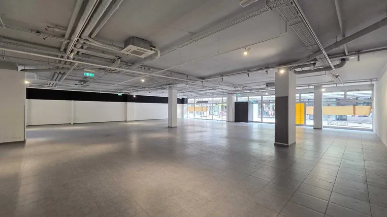 Großer, leerer Gewerberaum mit Fliesenboden und sichtbaren Deckeninstallationen, bereit für die individuelle Gestaltung.
