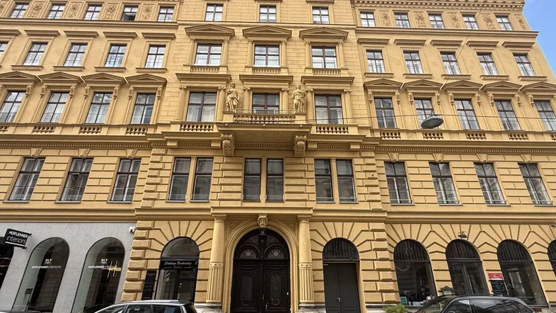 Historisches Gebäude mit gelber Fassade, vielen Fenstern und einem imposanten Eingangsbereich an einer Stadtstraße.