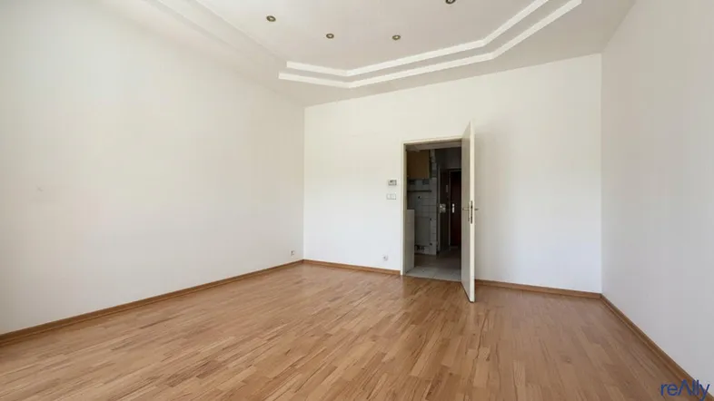 Helles, leeres Zimmer mit Parkettboden und einer dekorativen Deckenbeleuchtung, bereit zur Einrichtung.