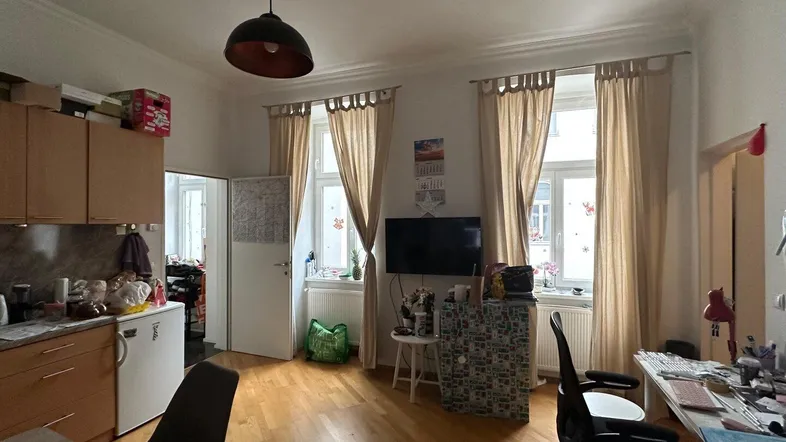 Heller Wohnbereich mit offener Küche, Parkettboden und großen Fenstern.
