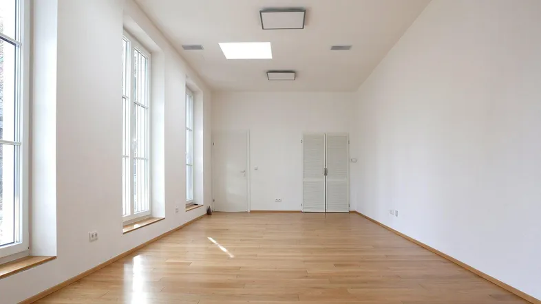 Helles, leeres Zimmer mit hohen Fenstern und Holzboden, ideal für vielfältige Nutzung.