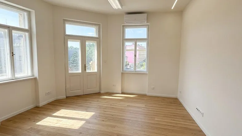 Heller, leerer Raum mit Holzboden, großen Fenstern und Klimaanlage, ideal für Wohn- oder Büronutzung.