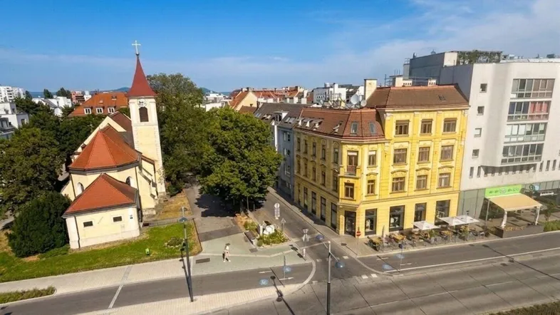 Panoramablick auf eine belebte Stadtstraße mit historischen Gebäuden und einer Kirche unter blauem Himmel.