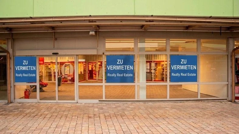 Eingangsbereich eines Geschäftsgebäudes mit großen Schaufenstern und "Zu Vermieten"-Schildern.