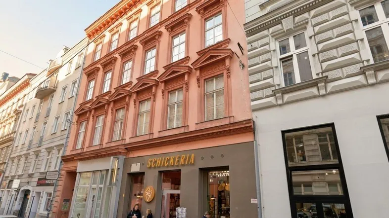 Historische Fassade eines Gebäudes mit Geschäften im Erdgeschoss und parkenden Autos auf der Straße.