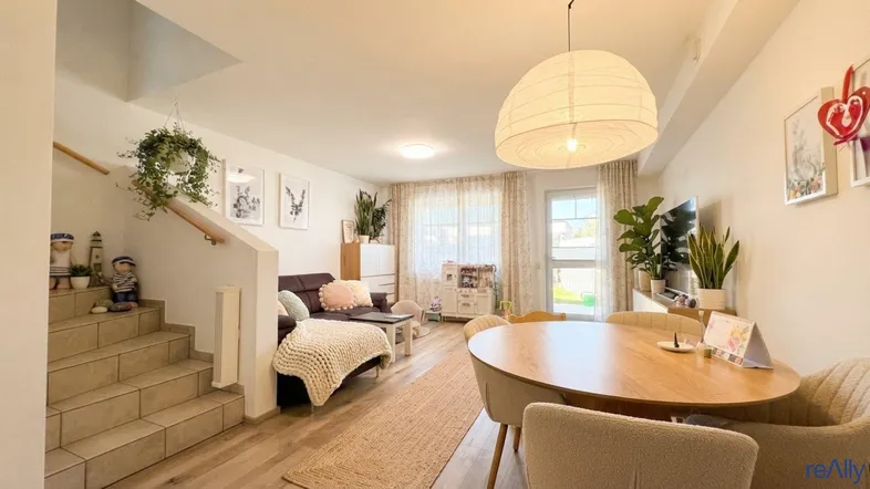 Helles Wohn- und Esszimmer mit Holzboden, Treppenaufgang und Blick ins Grüne.